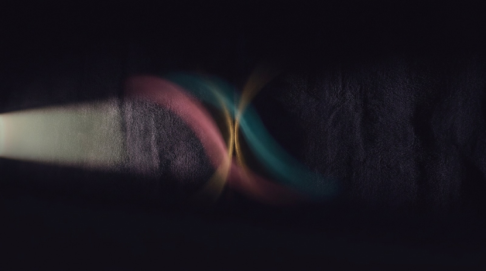 Two curved bands of colour, one rose and one teal, crossing in near-darkness with a
                thin warm seam of light where they meet.